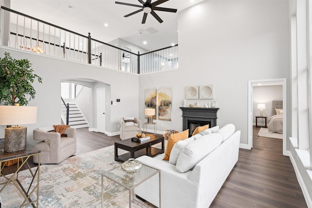 living room with dark hardwood / wood-style flooring, a towering ceiling, and ceiling fan