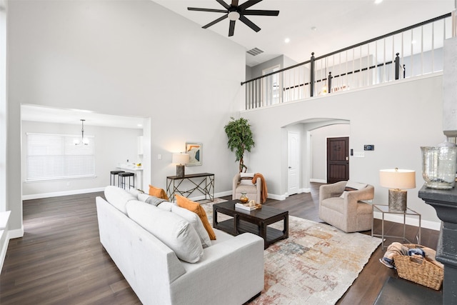 living room featuring dark wood-type flooring, ceiling fan with notable chandelier, and a high ceiling