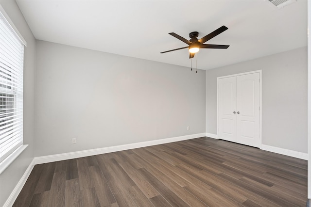 unfurnished bedroom with ceiling fan, multiple windows, dark wood-type flooring, and a closet