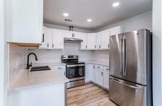 kitchen featuring decorative backsplash, appliances with stainless steel finishes, sink, light hardwood / wood-style flooring, and white cabinetry