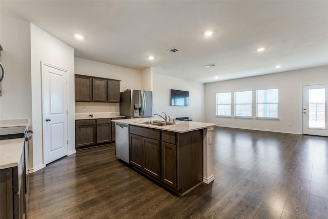 kitchen featuring appliances with stainless steel finishes, dark hardwood / wood-style flooring, dark brown cabinets, a kitchen island with sink, and sink