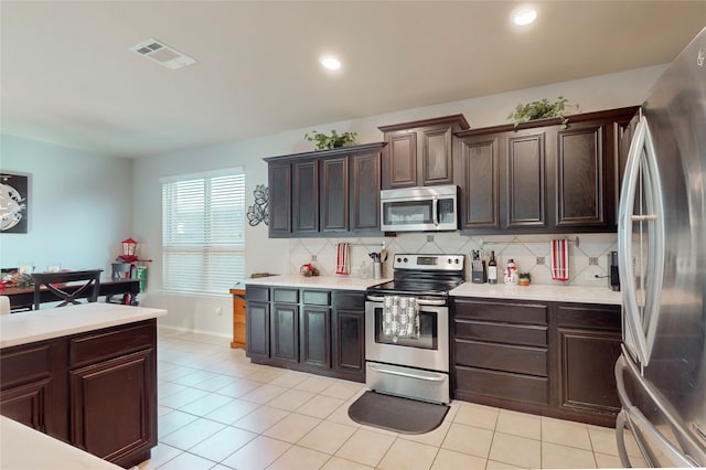 kitchen featuring dark brown cabinetry, backsplash, light tile patterned flooring, and appliances with stainless steel finishes