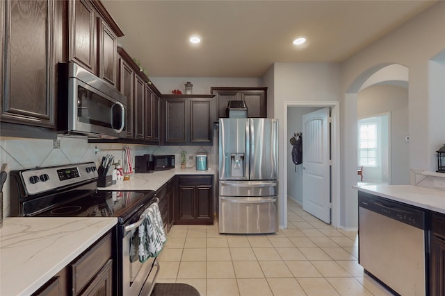 kitchen featuring dark brown cabinetry, backsplash, light tile patterned floors, and appliances with stainless steel finishes