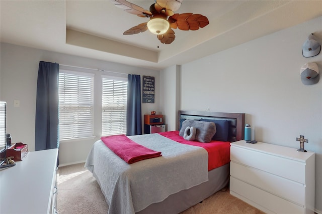 bedroom with a tray ceiling, light colored carpet, and ceiling fan