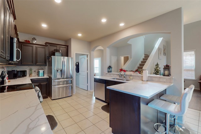 kitchen with sink, a breakfast bar area, dark brown cabinets, appliances with stainless steel finishes, and light stone countertops