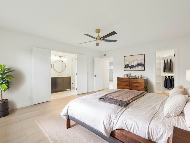 bedroom featuring light wood-type flooring, a walk in closet, a ceiling fan, and connected bathroom