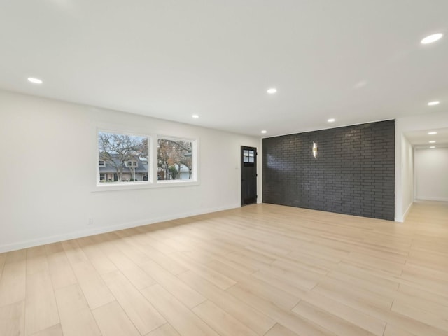 spare room featuring brick wall, light wood-style flooring, baseboards, and recessed lighting