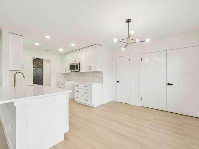 kitchen featuring white cabinets, light countertops, stainless steel microwave, and a sink