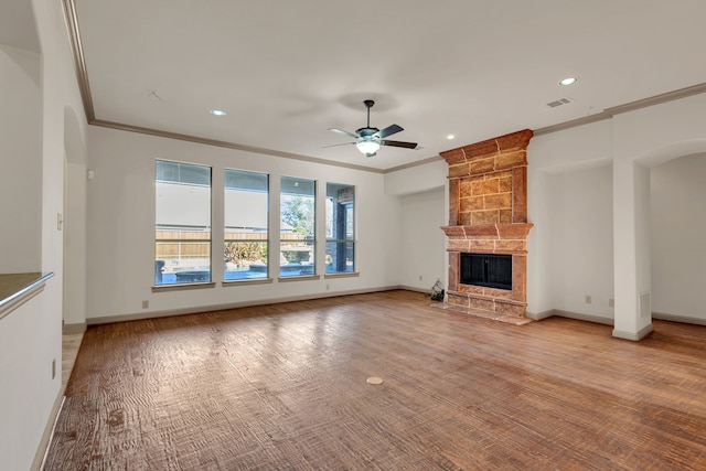 unfurnished living room featuring arched walkways, crown molding, a ceiling fan, a large fireplace, and baseboards