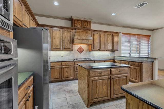 kitchen with stainless steel appliances, a kitchen island, brown cabinetry, dark countertops, and custom range hood