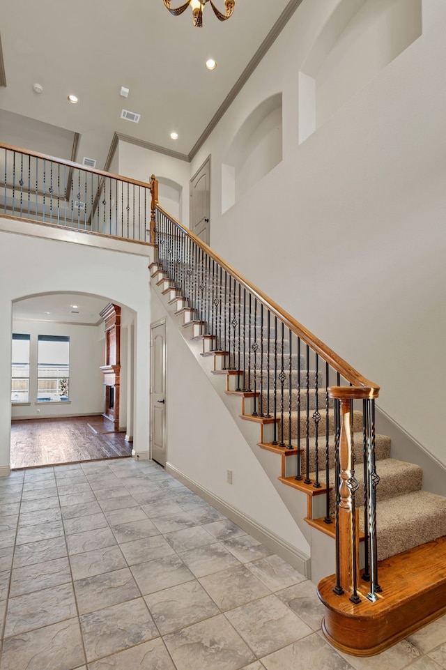 stairway with a towering ceiling and crown molding