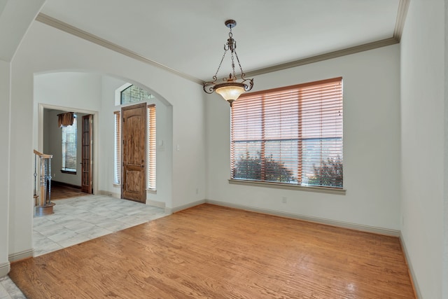 empty room featuring arched walkways, ornamental molding, plenty of natural light, and light wood-style floors