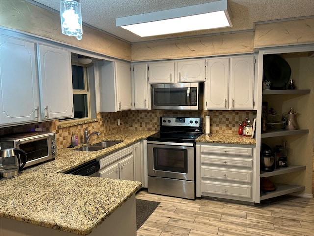 kitchen featuring open shelves, appliances with stainless steel finishes, a sink, light stone countertops, and a peninsula