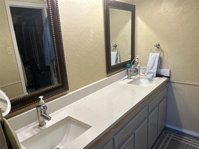 full bath with a sink, double vanity, a wainscoted wall, and a walk in closet