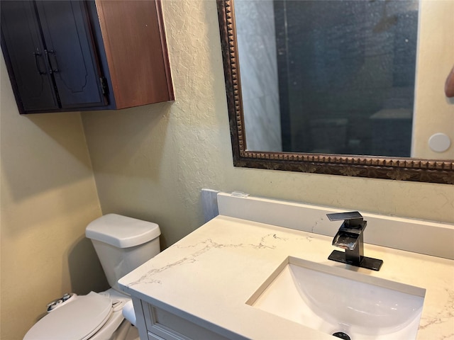 half bathroom with a textured wall, vanity, and toilet