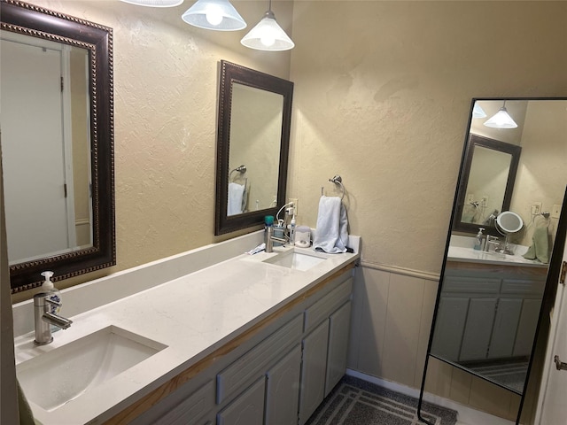 bathroom featuring a textured wall, a sink, and double vanity