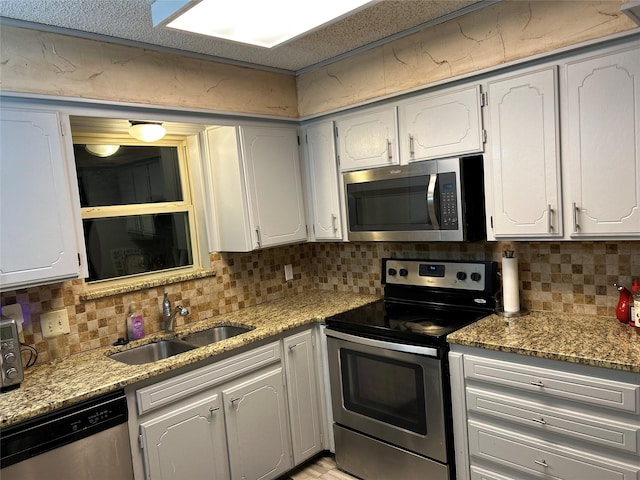 kitchen with light stone counters, appliances with stainless steel finishes, white cabinets, and a sink