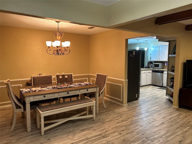 dining room with light wood-style flooring, a textured ceiling, and an inviting chandelier