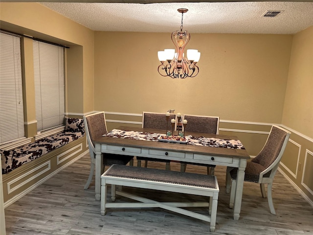 unfurnished dining area with visible vents, a textured ceiling, a chandelier, and wood finished floors