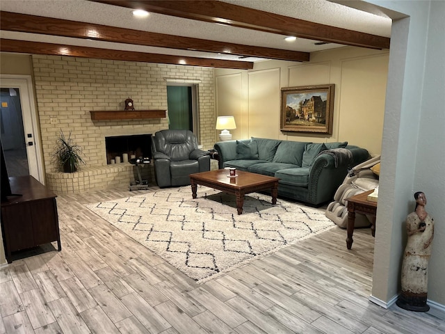 living room featuring light wood-style floors, a brick fireplace, beamed ceiling, and a textured ceiling