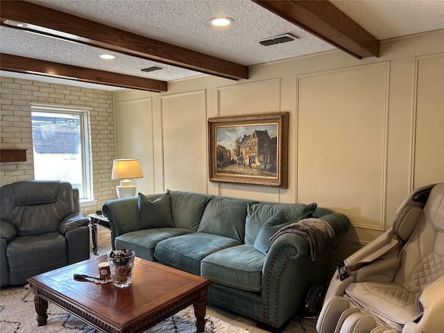 living area featuring a textured ceiling, beamed ceiling, visible vents, and a decorative wall