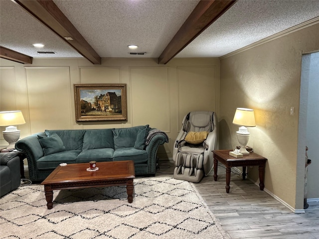 living room with beam ceiling, visible vents, a decorative wall, and a textured ceiling