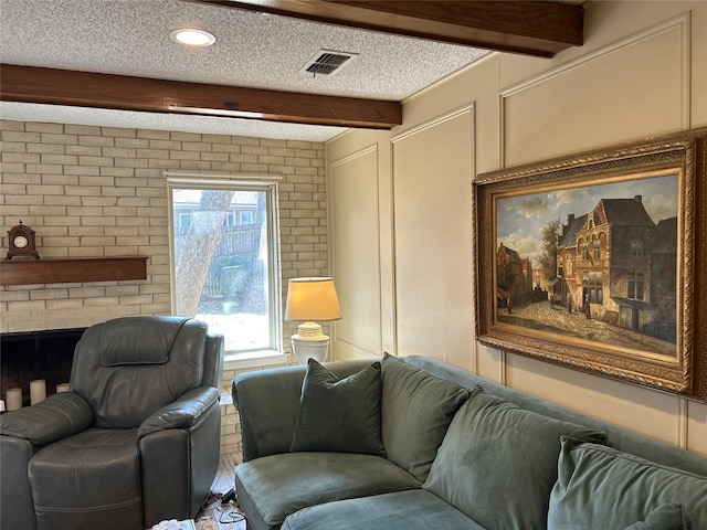 living area featuring a fireplace, visible vents, a decorative wall, a textured ceiling, and beamed ceiling