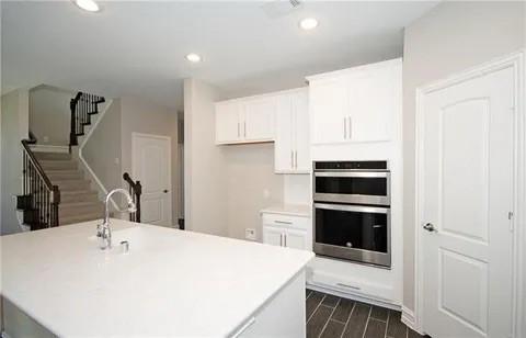 kitchen with white cabinetry, a center island with sink, and double oven