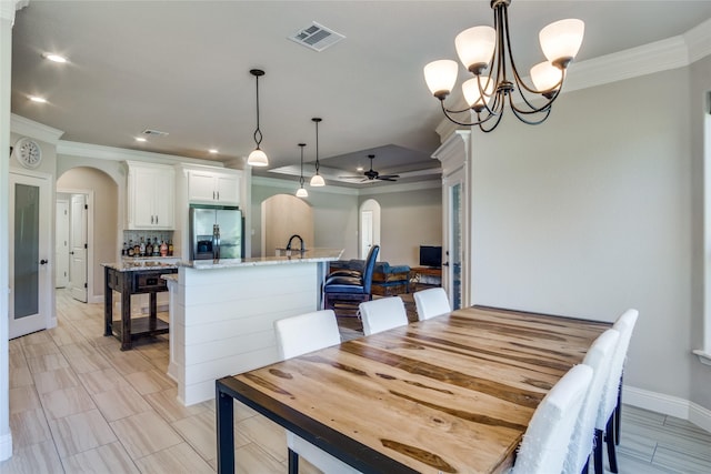 dining space with sink, crown molding, and ceiling fan with notable chandelier