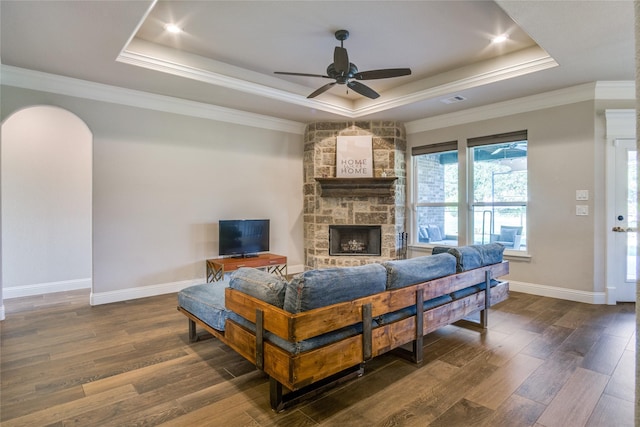 living room with dark hardwood / wood-style floors, ornamental molding, a tray ceiling, and a stone fireplace