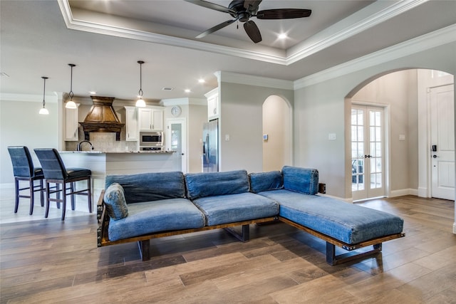 living room with ornamental molding, a raised ceiling, ceiling fan, and light wood-type flooring