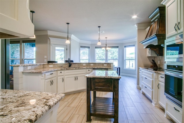 kitchen featuring sink, white cabinetry, hanging light fixtures, a center island, and light stone counters