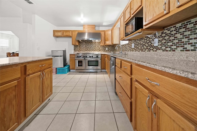 kitchen featuring wall chimney range hood, sink, appliances with stainless steel finishes, tasteful backsplash, and light stone counters