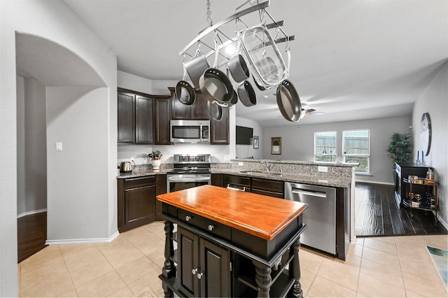 kitchen with dark brown cabinetry, sink, light tile patterned floors, appliances with stainless steel finishes, and kitchen peninsula