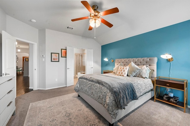 bedroom featuring ceiling fan, vaulted ceiling, ensuite bath, and dark colored carpet