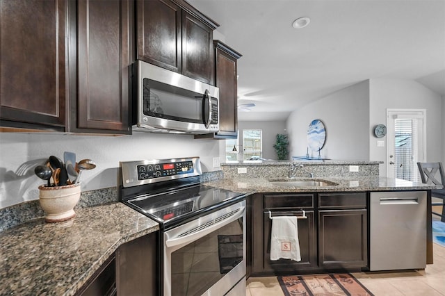 kitchen with sink, dark brown cabinets, dark stone countertops, appliances with stainless steel finishes, and kitchen peninsula