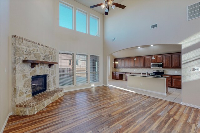 unfurnished living room featuring a fireplace, a towering ceiling, light hardwood / wood-style flooring, and ceiling fan