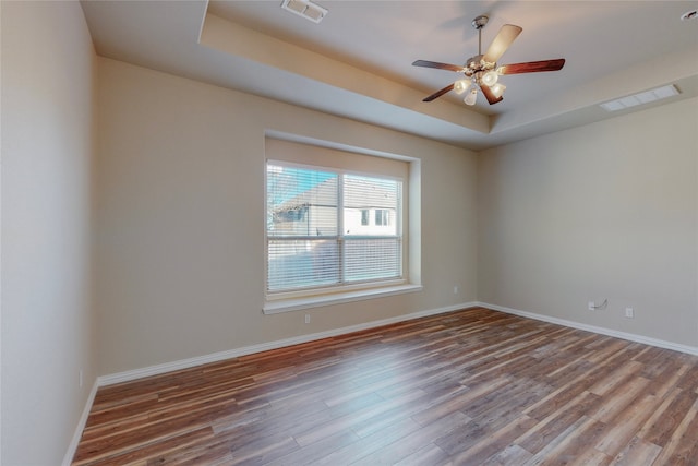 empty room featuring a raised ceiling, ceiling fan, and wood-type flooring