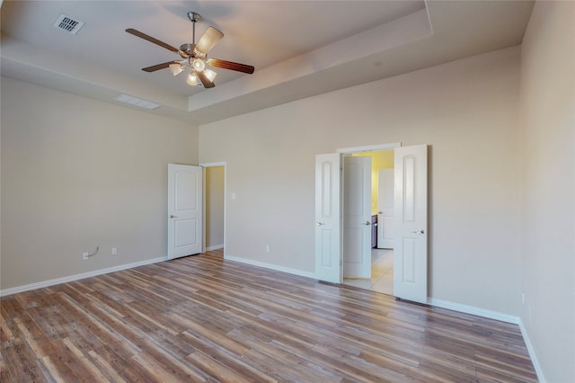 unfurnished bedroom featuring a high ceiling, a tray ceiling, ceiling fan, and light hardwood / wood-style floors