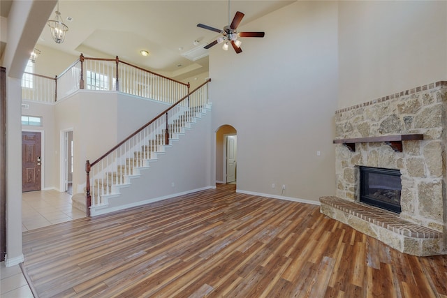 unfurnished living room with ceiling fan, a fireplace, light hardwood / wood-style floors, and a high ceiling