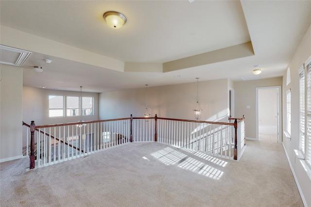 unfurnished room with a raised ceiling, light carpet, and an inviting chandelier