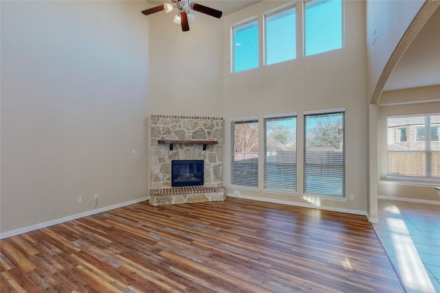 unfurnished living room with a stone fireplace, ceiling fan, a high ceiling, and hardwood / wood-style flooring