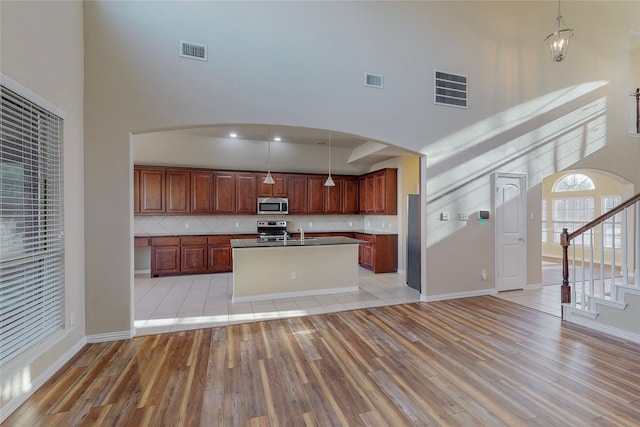 kitchen featuring a high ceiling, tasteful backsplash, decorative light fixtures, a kitchen island, and appliances with stainless steel finishes