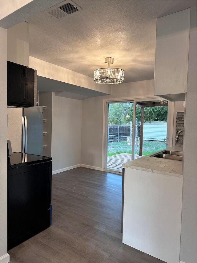 kitchen with dark wood-type flooring, sink, an inviting chandelier, stainless steel refrigerator, and black / electric stove