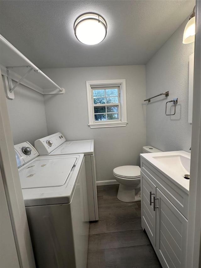 laundry room featuring washing machine and clothes dryer, sink, a textured ceiling, and dark hardwood / wood-style floors