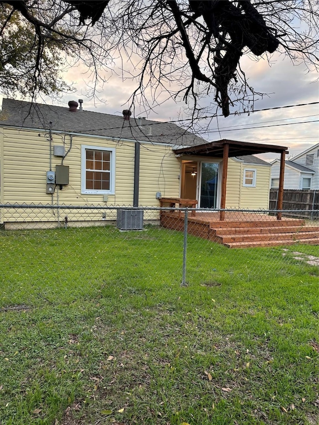 back house at dusk with central AC unit and a lawn