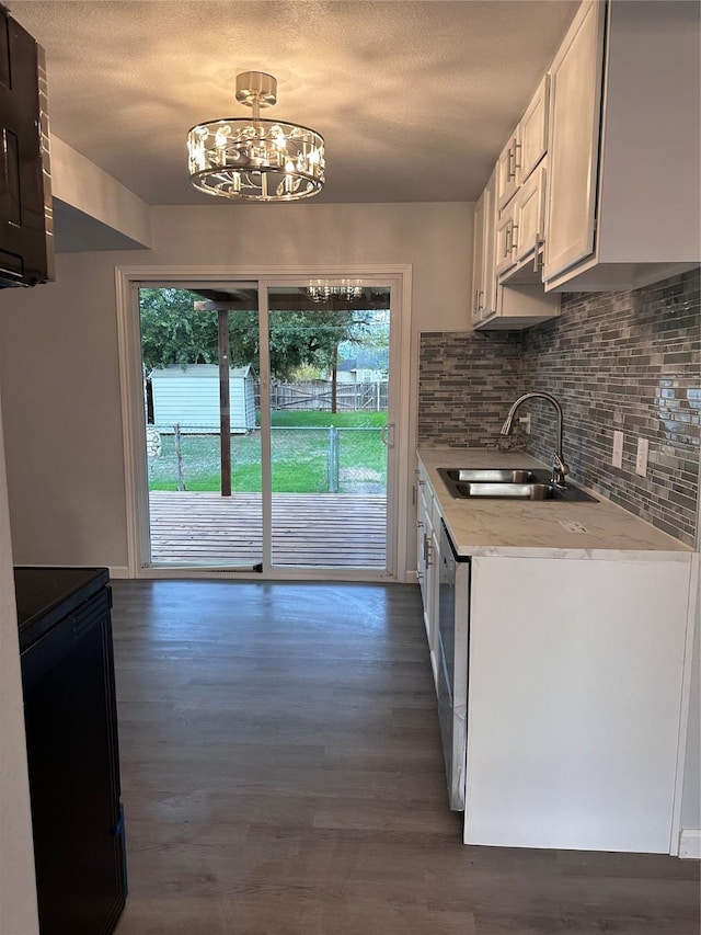 kitchen with sink, stainless steel dishwasher, dark hardwood / wood-style flooring, white cabinetry, and a chandelier