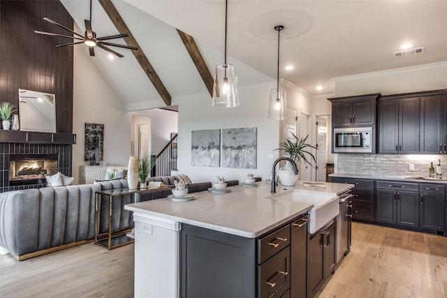 kitchen featuring a kitchen island with sink, hanging light fixtures, sink, appliances with stainless steel finishes, and beamed ceiling