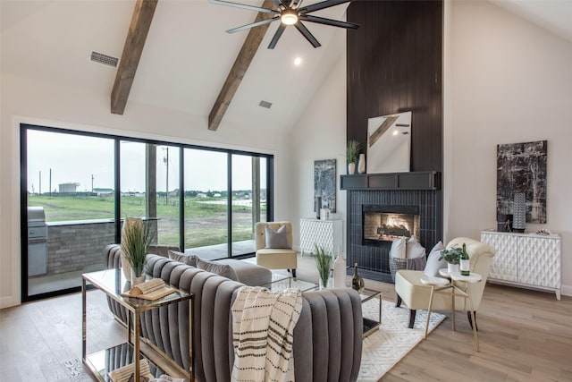 living room featuring high vaulted ceiling, light hardwood / wood-style flooring, ceiling fan, beamed ceiling, and a tiled fireplace