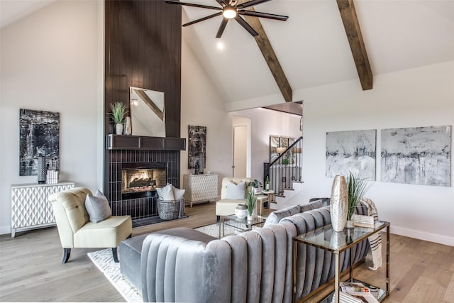 living room with high vaulted ceiling, light hardwood / wood-style flooring, ceiling fan, beamed ceiling, and a tiled fireplace